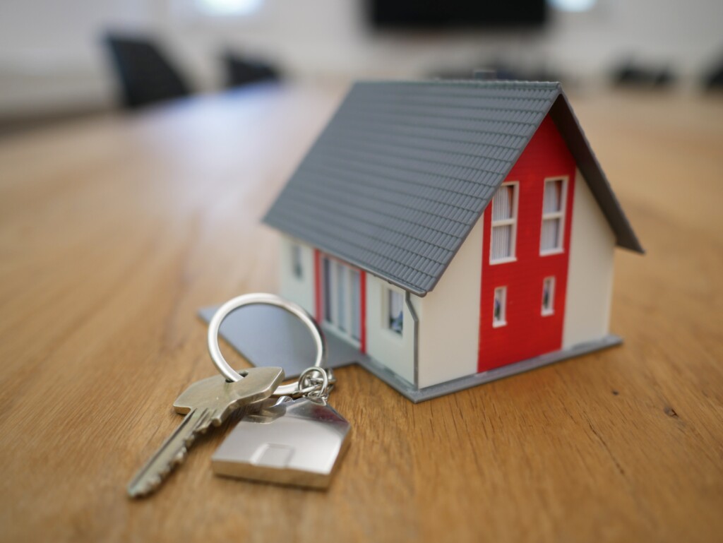 Photo of a small replica house on a desk with a set of real keys beside it.