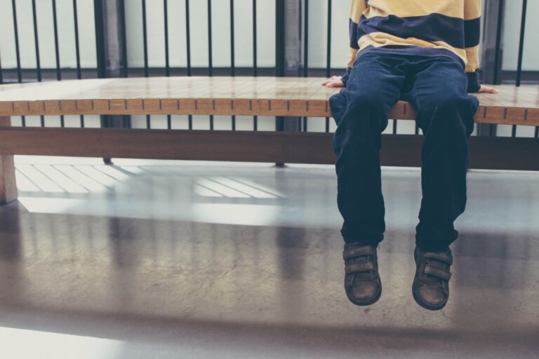 Photo of a child sitting on a bench, legs dangling in the air